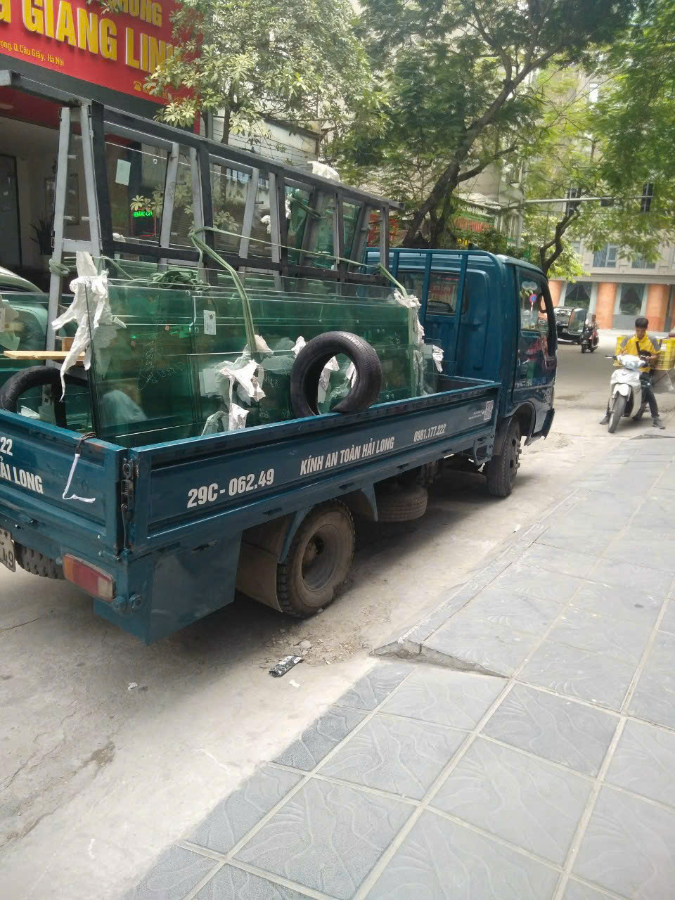 Xe chuyên dụng chở kính đến công trình trên tuyến phố nhiều cây xanh